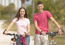 A teenage boy and girl walking with their bikes.