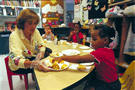 Image of a teacher serving orange slices to a little girl in the classroom