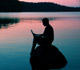 A person siting on a rock on a lake during sunset