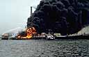 Docked ship on fire with plumes of black smoke rising