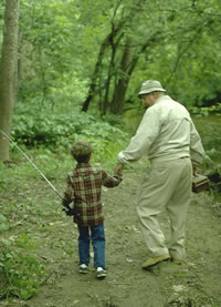 [photo:] A grandfather and his grandson hold hands as they walk through the woods with their fishing poles.