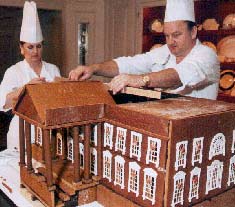 Photo: two chefs constructing a large gingerbread mansion.