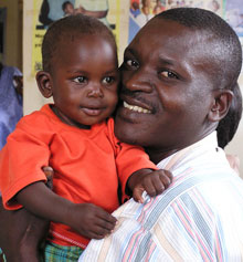 Photo of a father smiling and holding up his son, in Uganda.