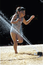 A young girl playing in a sprinkler.