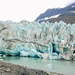 icy blue glacier flowing into water from mountain backdrop