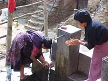 Photo of two people accessing water at a well.
