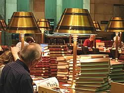 Reader at a table piled high with books.