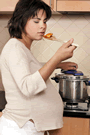 Image of a pregnant woman tasting food as she cooks
