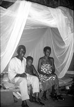 Photo of a family sitting under an insecticide-treated bednet to prevent malaria.