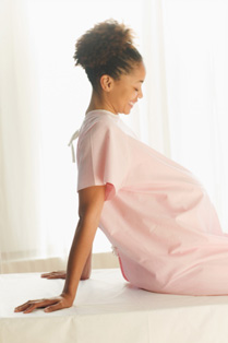 Image of pregnant African American woman, wearing exam gown and reclining.