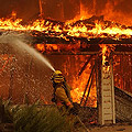 Firefighter extinguishing flames consuming a home.