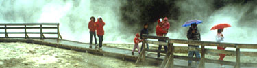 Visitors enjoy a stroll along a boardwalk near a thermal feature.