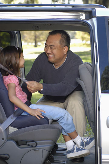 father securing child in a child car seat