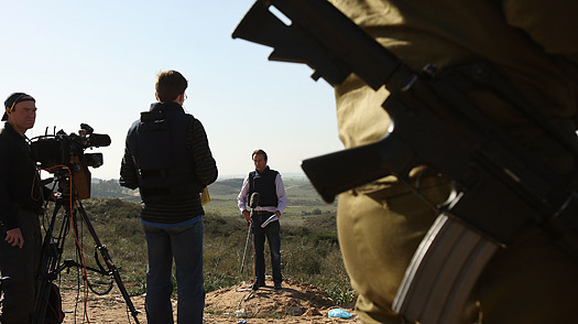 A television journalist delivers a report from the Israeli side of the Gaza border