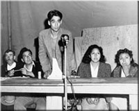 Three men and two women seated behind a table with a microphone in front of it.