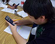 image of student sitting at his desk with a calculator