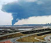 view of city horizon with a large plume of blue smoke rising over a highway