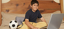 A boy sitting on his bed, using his laptop.