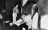 Two women stand over a child in bed.