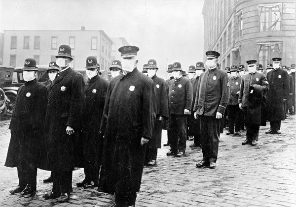 A black and white image of a row of policemen in uniform wearing white masks.