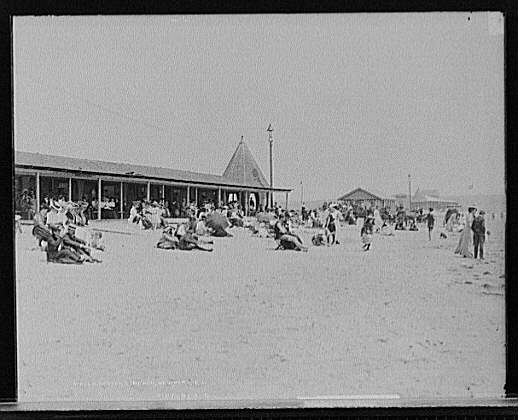 Numerous sunbathers sit or walk on the beach in a black and white image of Easton Beach in Newport, Rhode Island.  