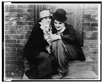 Charlie Chaplin and Edna Purviance have their arms around each other as they sit on a doorstep.