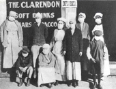 Men and women stand and sit in front of the Clarendon Store wearing masks. 
