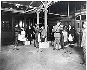 Immigrants stand in three lines.  A PHS officer stands at the head of each line.  The officers are examining the immigrants by checking their eyes for trachoma.