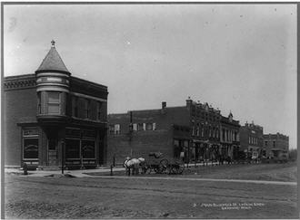 Main Street on small town.  Horse drawn carriages lined up along several two story building.