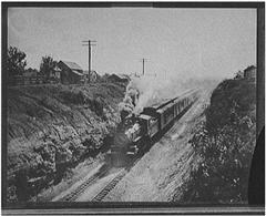 Railroad train in motion between two mountains lined with houses.