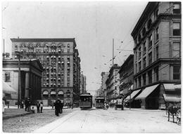 Market street with pedestrians waiting for street car.  Street cars coming in both directions. Urban scene.