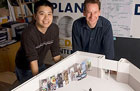 Photo: male student and male professor smiling over a model of state fair pavilion