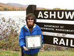 Image of woman holding award for trail in front of trail sign.