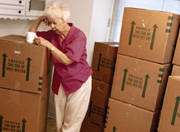Photo of elderly woman standing amid packing boxes