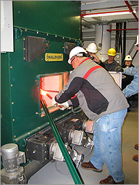 Photo of a man wearing a white hard hat lighting the flare to start a boiler.