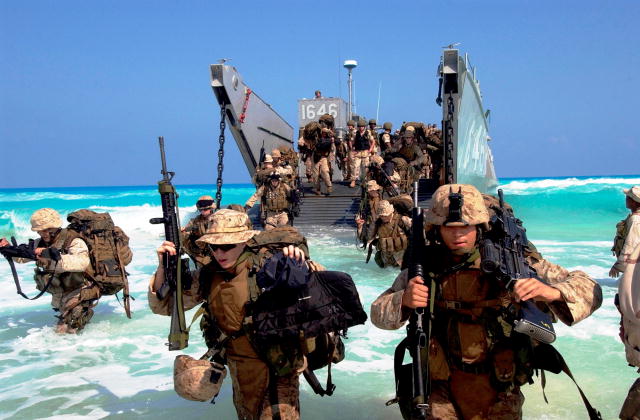 Photo of a group of soldiers disembarking a Landing Craft Utility and wading through the water.