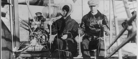 Katharine Wright takes her first flight in February 1909 in Pau, France, seated next to her brother, Wilbur, who developed the airplane with brother Orville, standing at left; from "The Dream of Flight."