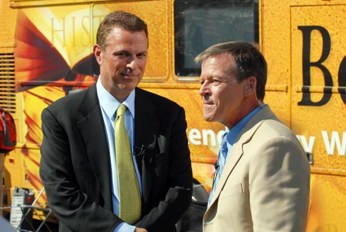 Two men standing near a yellow vehicle.