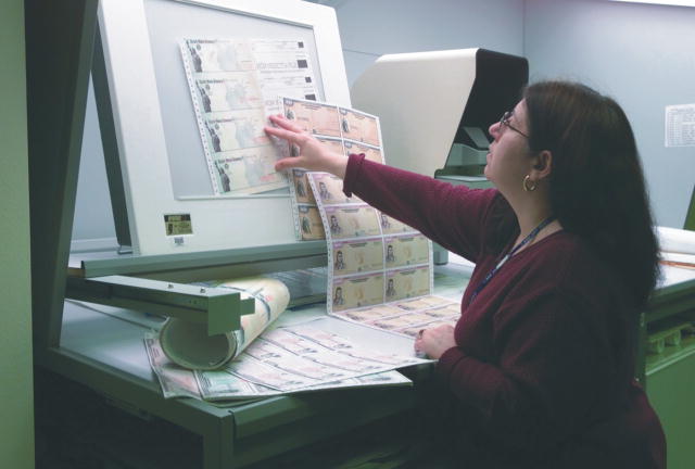 A worker carefully checks the quality of recently printed savings bonds.