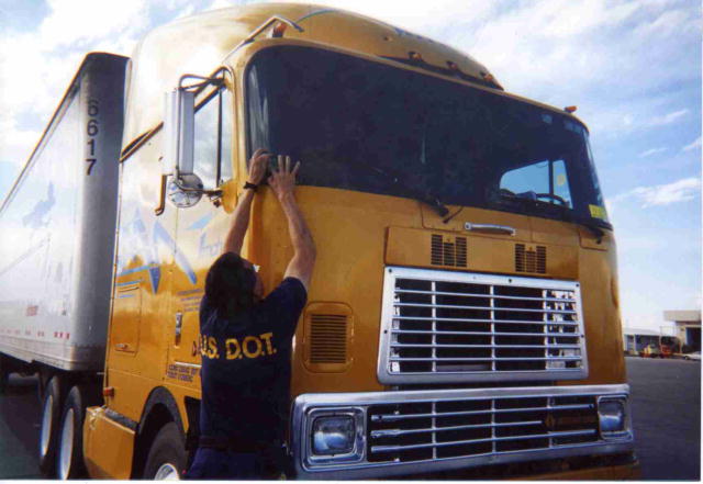 A DOT safety inspector applies a decal to the windshield of a semi-tractor.
