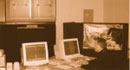 A man is sitting at one of two computers in a laboratory. A large screen is on the wall in front of him showing a computer program that models traffic flow.