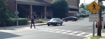 A car is stopped at a crosswalk while a pedestrian crosses the street.