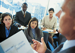 Photo of a group of people listening to a person with a report in hand