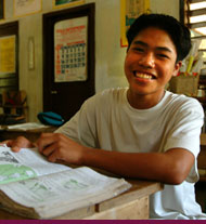 A youth smiles as he looks up from a book