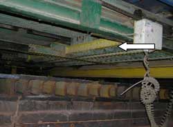 A traveling bar under the stacker moves an alignment chain. Arrow shows bar and direction of travel.