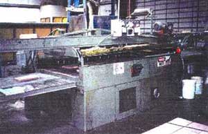 The glue press operates on an automatic cycle, with a conveyor running beneath a glue roller and into the press.
