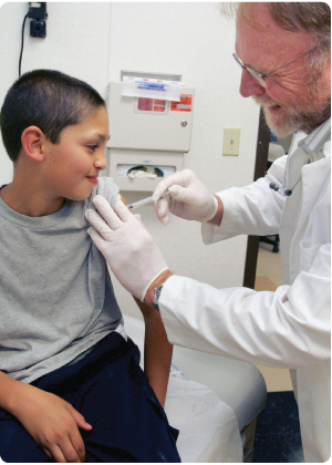 photo of a boy getting a vaccination from a nurse, both are smiling.
