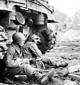 Two U.S. soldiers in Gaich, Germany, pause for a cigarette behind a tank on December 11, 1944. 