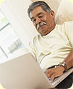 A man, relaxing, looking at his laptop.