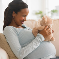 Image of pregnant African American woman looking at a teddy bear.